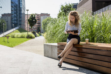 Businesswoman sitting on bench using digital tablet - MAUF000700