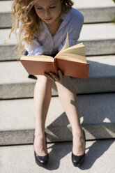 Frau sitzt auf einer Treppe und liest ein Buch - MAUF000708