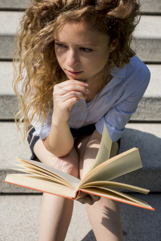 Frau sitzt auf einer Treppe und liest ein Buch, lizenzfreies Stockfoto