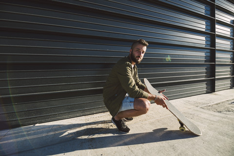 Mann mit Skateboard hockt vor einer Fassade, lizenzfreies Stockfoto