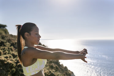 Spain, Asturias, sportswoman on the coast, stretching arms - MGOF002164