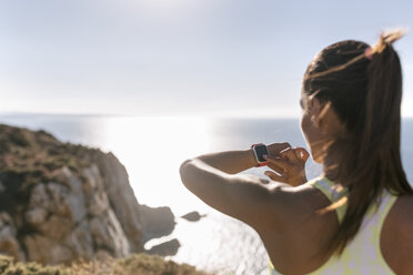 Spanien, Asturien, Sportlerin an der Küste, Blick auf die Smartwatch - MGOF002181