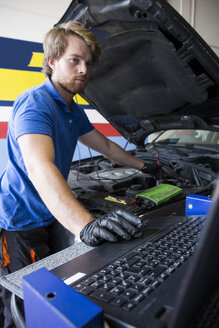 Mechaniker, der einen Automotor repariert, während er einen Computer in seiner Werkstatt benutzt - ABZF000939