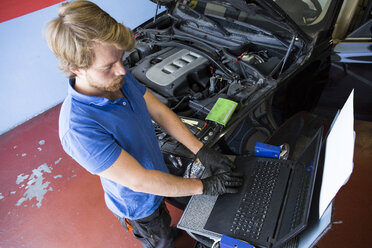 Mechaniker, der einen Computer benutzt, während er ein Auto repariert - ABZF000951