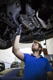 Mechaniker, der in seiner Werkstatt ein aufgehängter Wagen repariert - ABZF000953