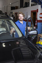 Lächelnder Mechaniker mit einem Auto in seiner Werkstatt - ABZF000966