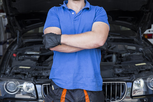 Mechaniker steht mit verschränkten Armen in seiner Autowerkstatt - ABZF000969