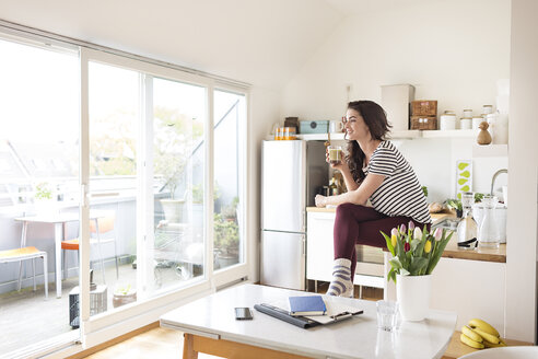 Smiling young woman relaxing in kitchen - PESF000268