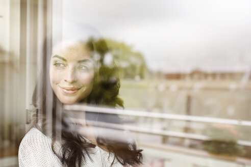 Lächelnde junge Frau schaut aus dem Fenster - PESF000277