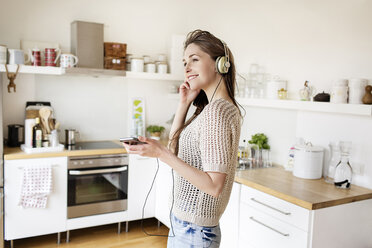 Lächelnde junge Frau in der Küche beim Musikhören - PESF000278