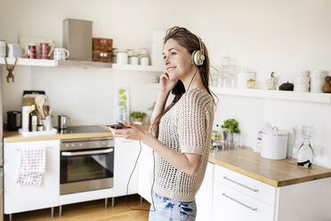 Smiling young woman in kitchen listening to music - PESF000278