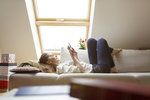 Entspannte Frau auf der Couch liegend, die ein Mobiltelefon benutzt - PESF000286