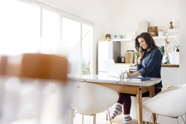 Smiling young woman at home using cell phone laptop - PESF000287