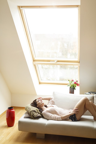 Entspannte Frau liegt auf der Couch und schaut aus dem Fenster, lizenzfreies Stockfoto