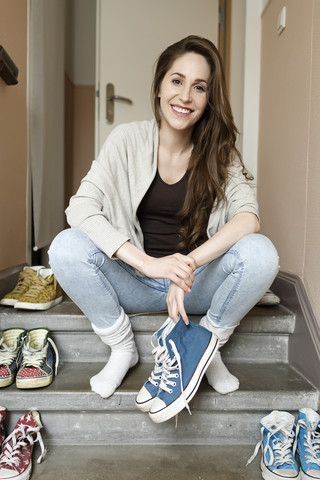 Lächelnde junge Frau sitzt auf einer Treppe und hält Turnschuhe, lizenzfreies Stockfoto