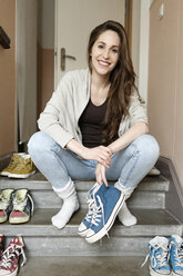 Lächelnde junge Frau sitzt auf einer Treppe und hält Turnschuhe - PESF000307