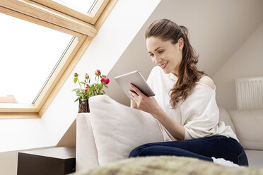 Lächelnde Frau sitzt auf der Couch und benutzt ein digitales Tablet - PESF000317
