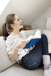 Glückliche Frau sitzt auf der Couch und liest ein Buch - PESF000319