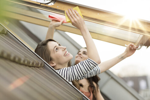 Lächelnde junge Frau, die ein Dachfenster putzt - PESF000337