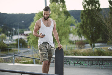 Junger Mann im Skatepark schaut auf sein Handy - RAEF001359