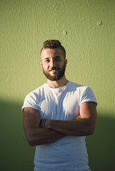 Portrait of smiling man with arms crossed in front of green background - RAEF001361