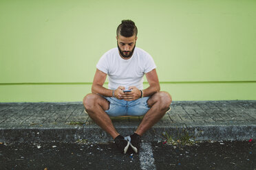 Man sitting on his skateboard at carb text messaging - RAEF001367