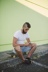 Man sitting on his skateboard at carb text messaging - RAEF001368