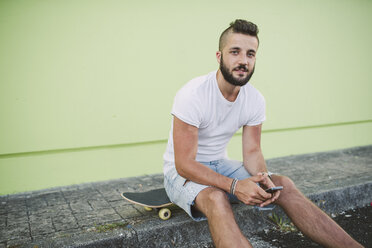Porträt eines Mannes mit Smartphone, der auf seinem Skateboard im Auto sitzt - RAEF001369