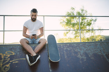 Skateboarder benutzt Smartphone in einem Skatepark - RAEF001378