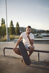 Porträt eines Skateboarders, der in einem Skatepark sitzt - RAEF001389