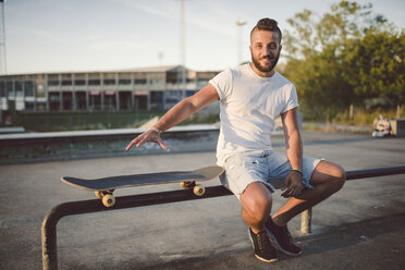 Porträt eines Skateboarders, der in einem Skatepark sitzt - RAEF001390