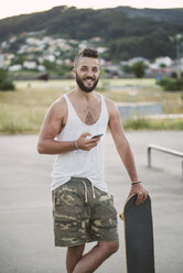 Porträt eines lächelnden Mannes mit einem Skateboard und einem Smartphone - RAEF001394