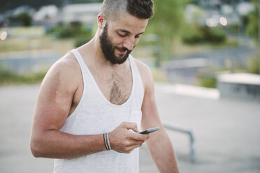 Young man with shaved head looking at cell phone - RAEF001395