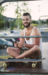 Portrait of smiling skateboarder with smartphone - RAEF001400