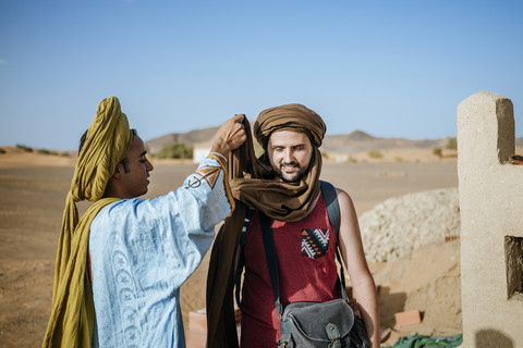 Berberführer hilft Touristen beim Wickeln eines Turbans, lizenzfreies Stockfoto