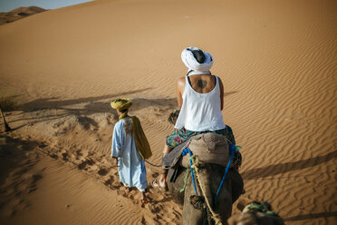Frau reitet auf einem Kamel in der Wüste mit Berberführer - KIJF000699