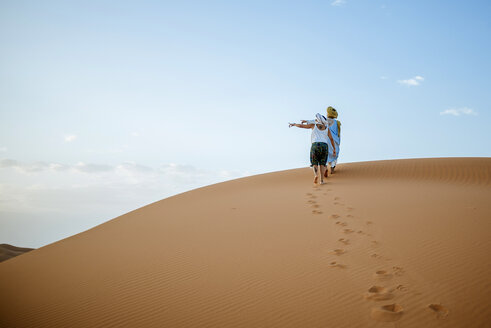 Berbermann und -frau, die in der Wüste spazieren gehen, nach links zeigend - KIJF000705