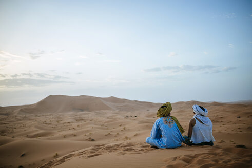 Frau sitzt mit Berberführer in der Wüste und beobachtet den Sonnenuntergang - KIJF000710