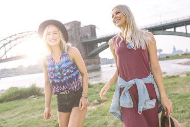 Zwei lächelnde junge Frauen gehen am Flussufer spazieren - MADF001064