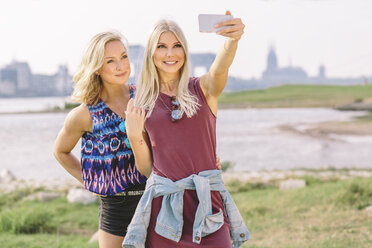 Two smiling young women taking a selfie at riverbank - MADF001068