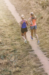 Two young women running on field path - MADF001091