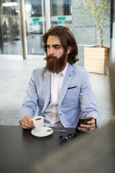 Stylish businessman holding cell phone in a cafe - MAUF000750