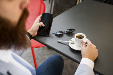 Stylish businessman holding cell phone in a cafe - MAUF000751