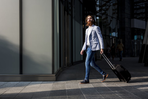 Stylish businessman walking with suitcase outdoors stock photo
