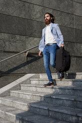 Stylish businessman walking with suitcase on stairs outdoors - MAUF000757