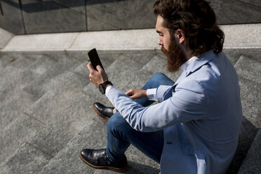 Stylish businessman using cell phone on stairs outdoors - MAUF000761