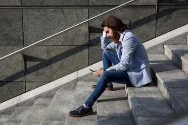 Stylish businessman using cell phone on stairs outdoors - MAUF000762