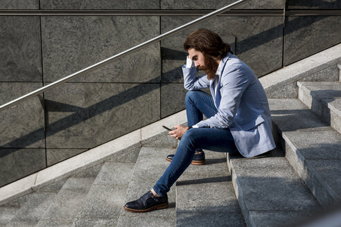 Stilvoller Geschäftsmann benutzt Handy auf einer Treppe im Freien - MAUF000762