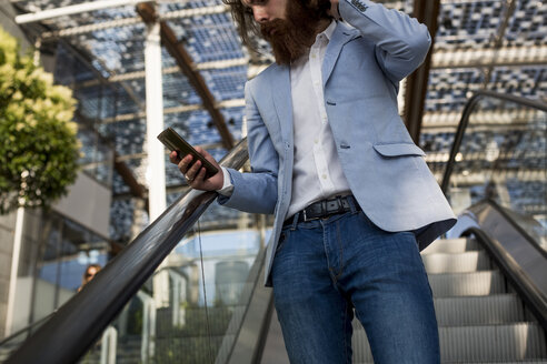 Stilvoller Geschäftsmann benutzt Handy auf Rolltreppe - MAUF000766