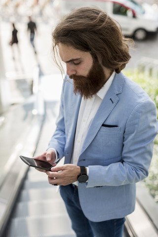 Stilvoller Geschäftsmann benutzt Handy auf Rolltreppe, lizenzfreies Stockfoto